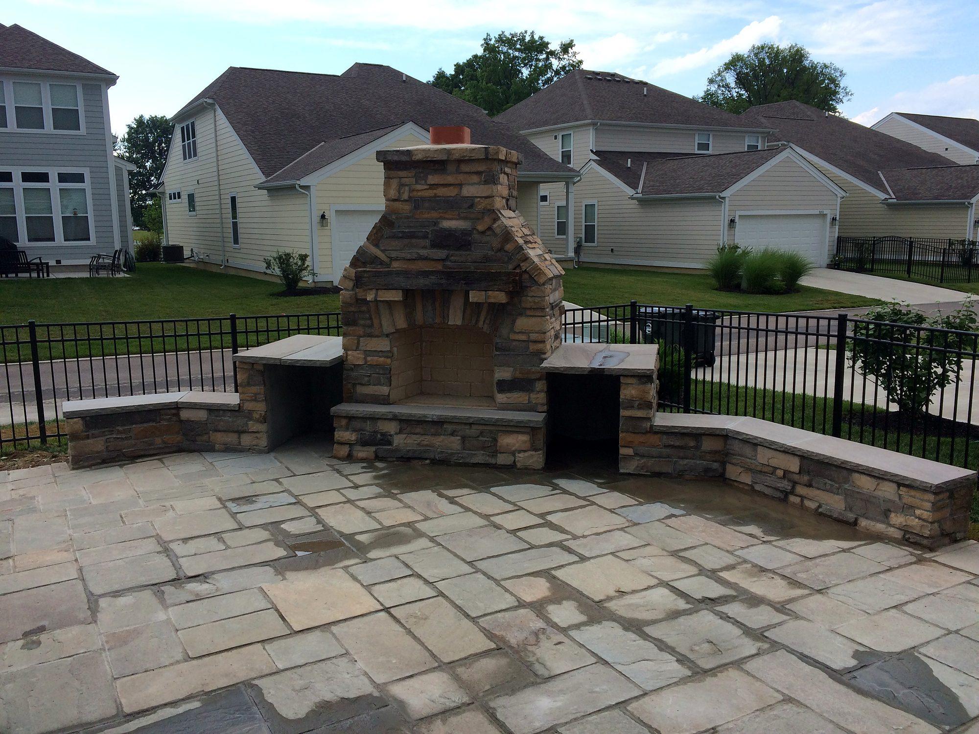 Paver patio with stacked-stone outdoor fireplace, wood storage boxes and seat walls