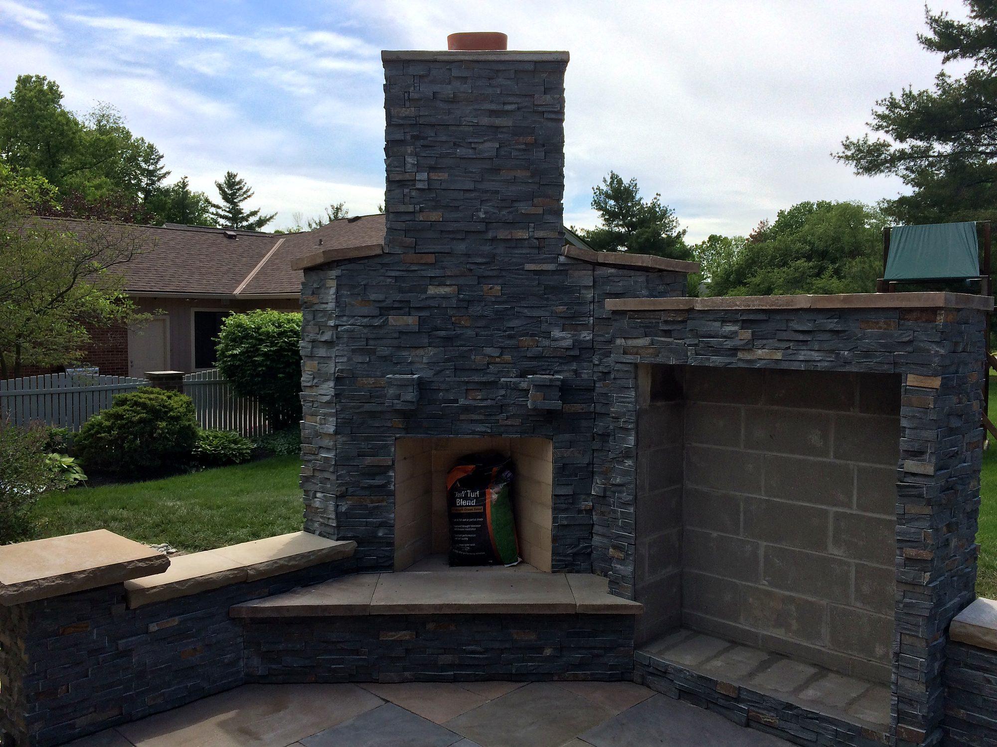 Charcoal stacked-stone outdoor fireplace with built-in wood storage and seat wall