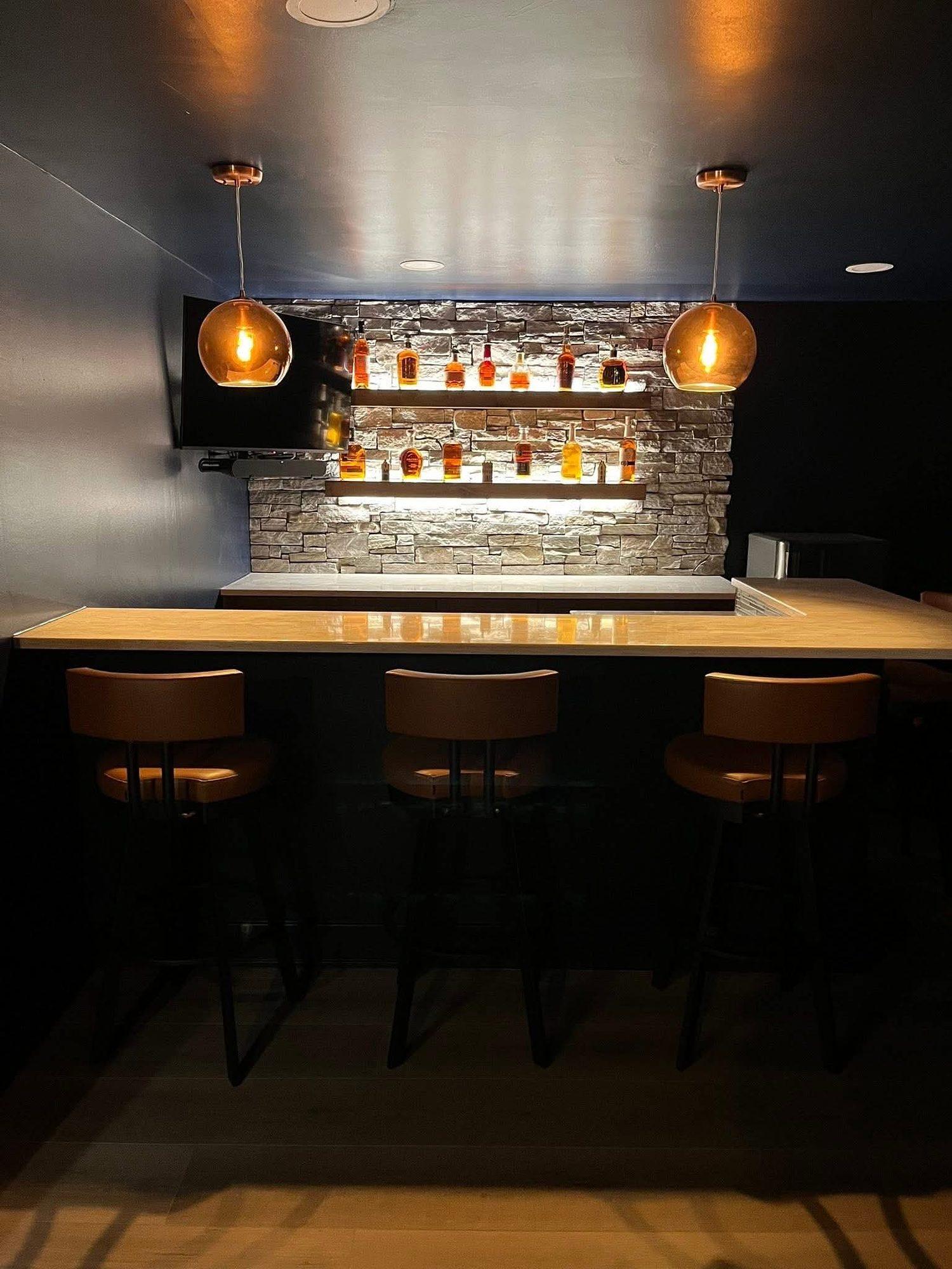 Basement bar with leather stools, copper pendant lights and a lighted stone backsplash