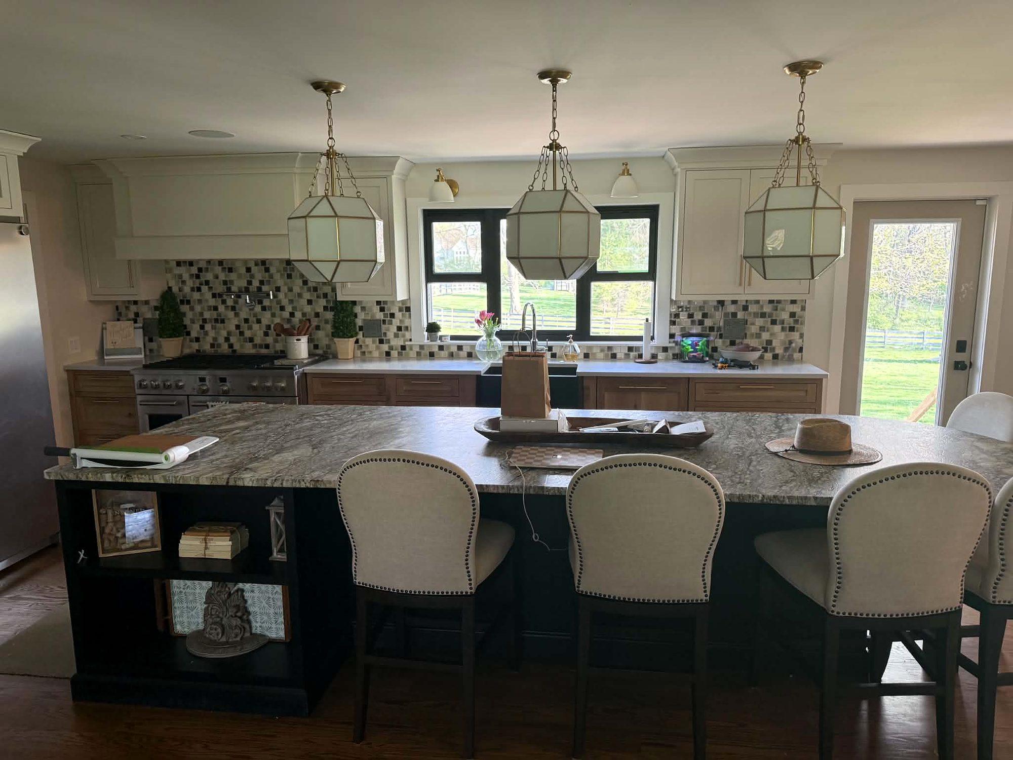 Kitchen remodel with a large stone-topped island, upholstered bar stools, glass lantern pendants and a mosaic tile backsplash